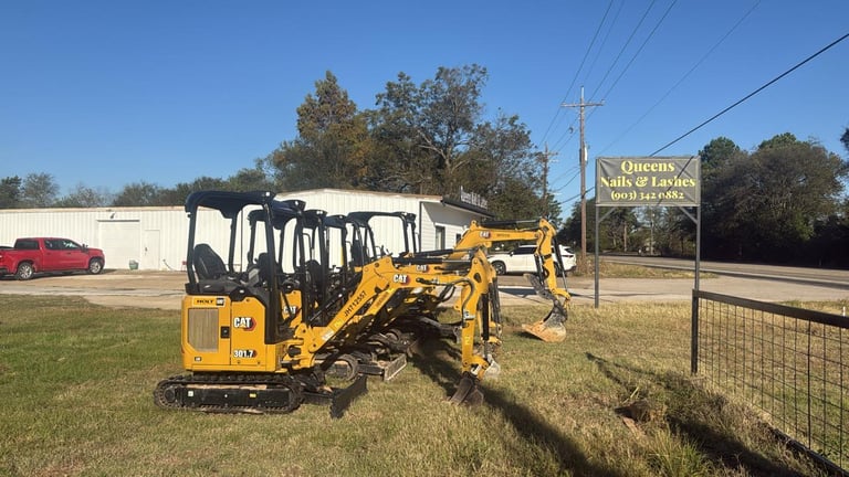 Yellow mini excavator parked on grass next to a fence at a commercial property during daytime
