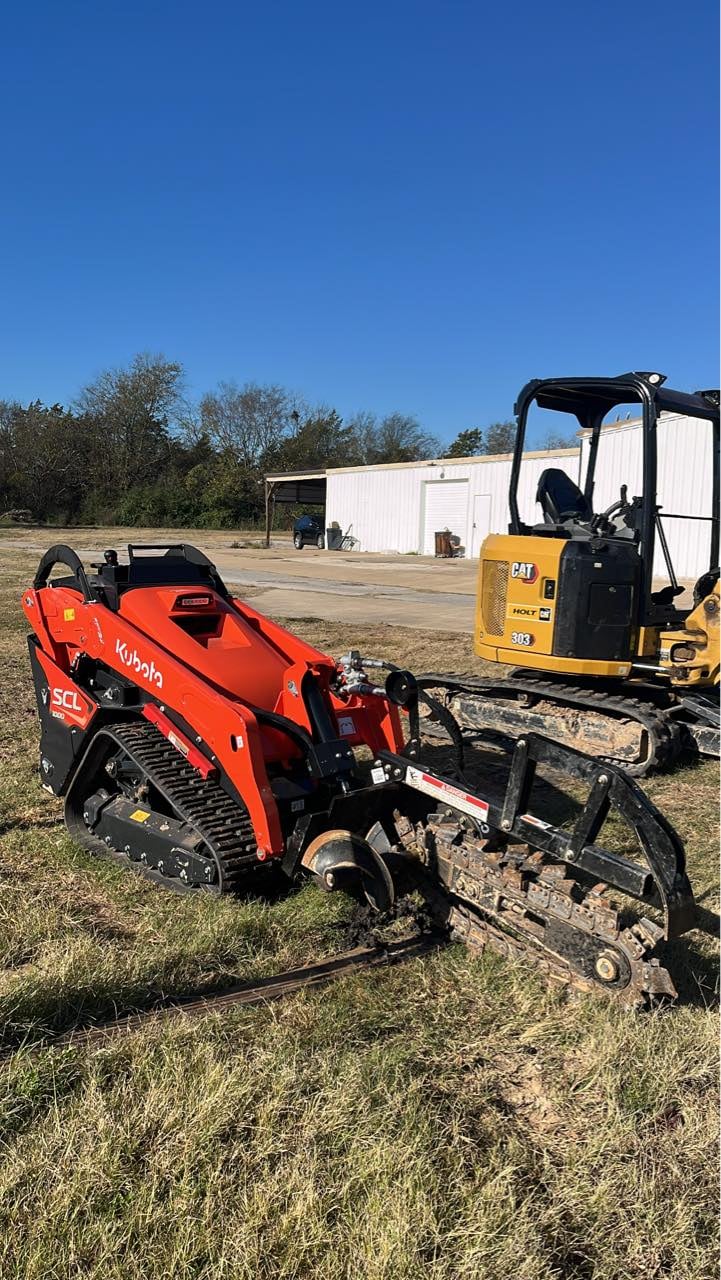 Red Kubota skid steer loader with attachment next to yellow excavator on outdoor job site