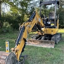 Yellow compact excavator parked on grass near trees in outdoor setting