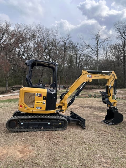 Yellow CAT mini excavator with black track and bucket arm parked on dirt ground