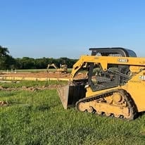Yellow skid-steer loader parked in a harvested agricultural field under clear blue sky