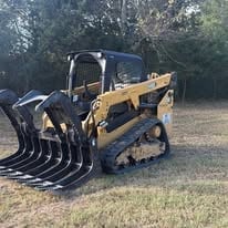 Yellow Caterpillar skid steer loader with front-mounted grapple bucket attachment parked outdoors