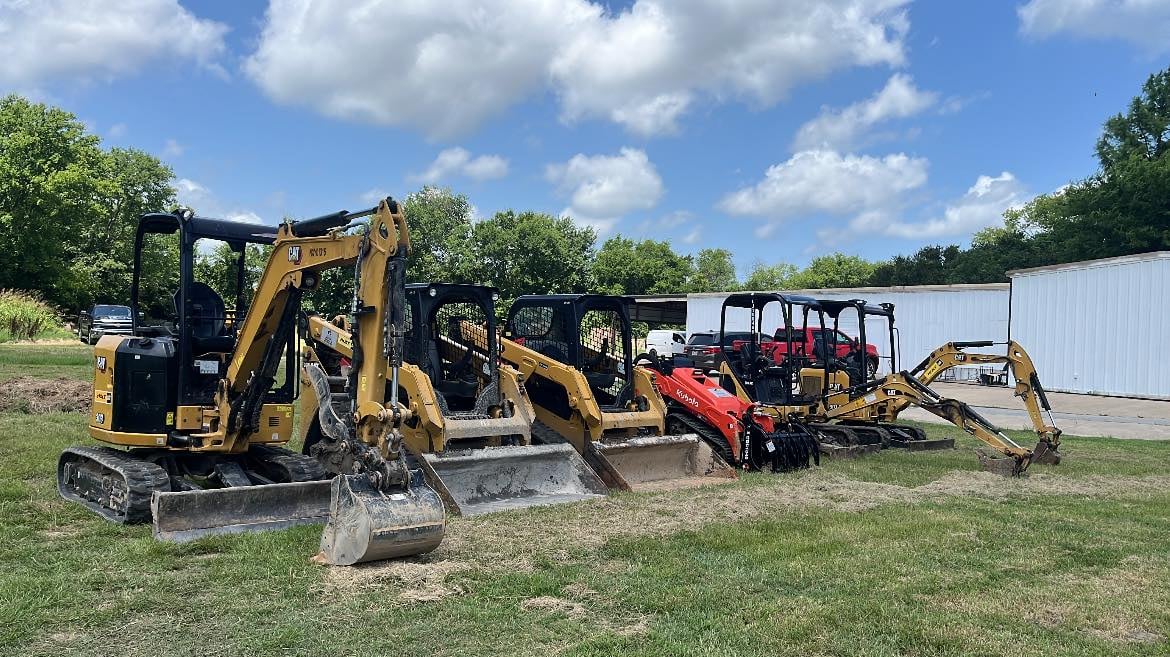 Construction equipment yard with yellow and red excavators and machinery parked on grass near a metal building