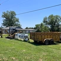 Truck with attached wooden trailer parked on grass field with trees and power lines in background